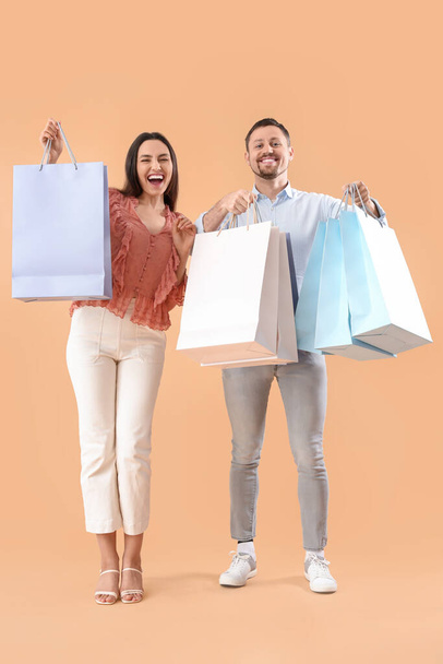 Happy young couple with shopping bags on beige background - Photo, Image
