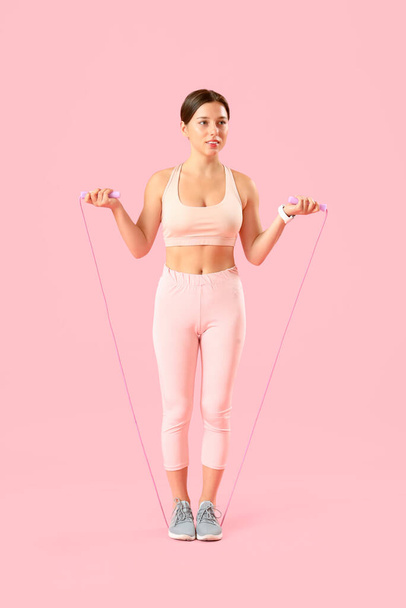 Mujer joven deportiva con cuerda de salto sobre fondo rosa - Foto, Imagen
