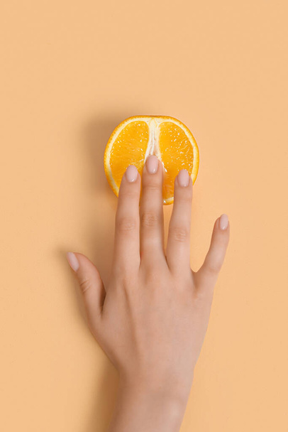 Main féminine avec la moitié de l'orange frais sur fond beige. Concept d'éducation sexuelle - Photo, image