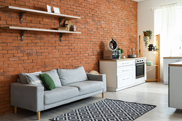 Интерьер современной открытой кухни с серым диваном и кофеваркой на прилавке - Фото, изображение