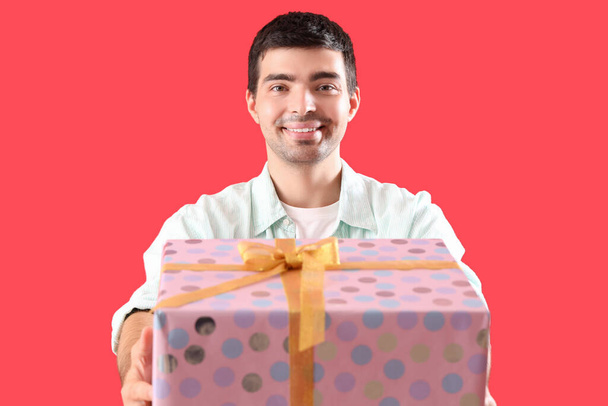 Ευτυχισμένος νεαρός άνδρας με δώρο γενεθλίων σε κόκκινο φόντο - Φωτογραφία, εικόνα