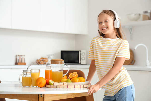 Pieni tyttö kuulokkeet tuoretta mehua ja eri sitruksia pöydässä keittiössä - Valokuva, kuva