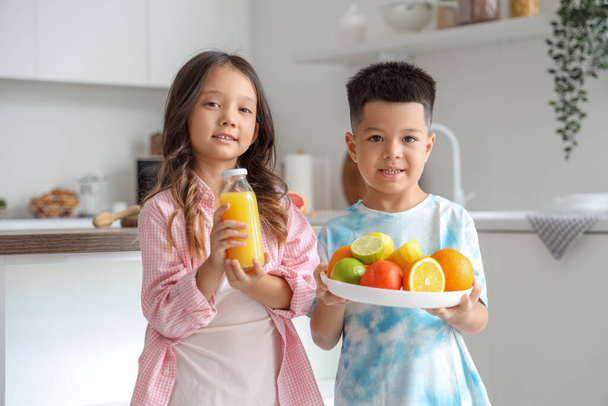 Küçük Asyalı çocuklar ellerinde taze meyve suyu şişesi ve farklı sitruslarla mutfaktalar. - Fotoğraf, Görsel