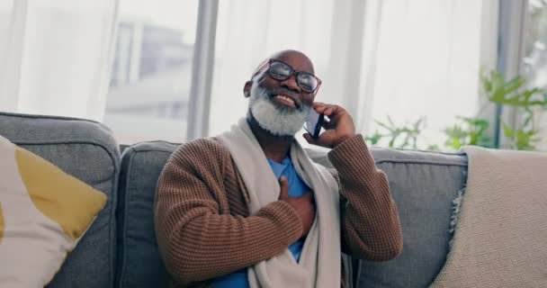 Σπίτι, τηλέφωνο και ηλικιωμένος στον καναπέ, χαμόγελο και σύνδεση με επικοινωνία, συνομιλία και δίκτυο. Αφρικανός, συνταξιούχος ή τύπος με έξυπνο τηλέφωνο, συζήτηση ή συνταξιοδότηση σε ένα σαλόνι. - Πλάνα, βίντεο