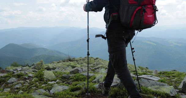 Un viaje en las montañas, un turista va con una mochila y palos, viaja a través del terreno rocoso de las altas montañas, excursionistas independientes y solitarios en las rocas. - Foto, Imagen