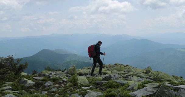 A trip in the mountains, a tourist goes with a backpack and sticks, travels through the rocky terrain of high mountains, independent, lone hikers on rocks. - Photo, Image