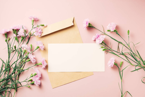 Λευκά ευχετήρια κάρτα και όμορφα άνθη γαρύφαλλου στο ροζ φόντο. - Φωτογραφία, εικόνα