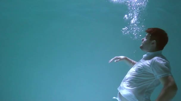 De man in kleren wentelt zich onder water. Hij zinkt in het water.. - Video