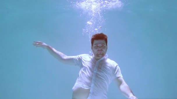 De man in kleren wentelt zich onder water. Hij zinkt in het water.. - Video