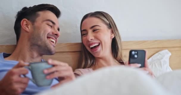 Couple, coffee and phone in bed, smile and comic laugh for meme, post or web blog in morning on vacation. Man, woman and smartphone to watch funny video, movie or reading notification on social media. - Footage, Video