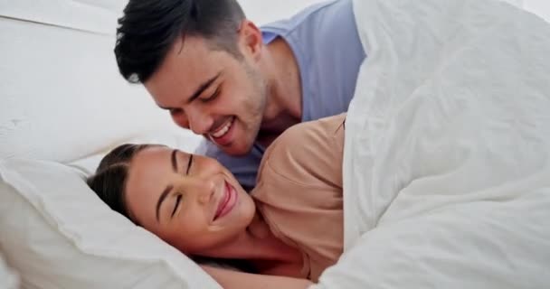 Kiss, cuddle and couple relaxing in bed for romance or bonding together on a weekend morning. Happy, love and young man and woman with intimate moment for resting in bedroom at home in Australia - Footage, Video