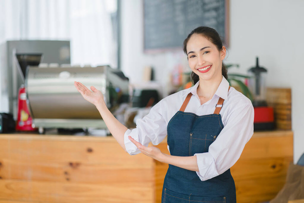Portret van een lachende jonge Aziatische barista wachtend op klanten bij koffiewinkel.Succesvolle kleine ondernemer in casual dragen schort staan bij de ingang - Foto, afbeelding