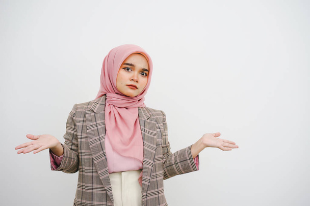Όμορφη νεαρή μουσουλμάνα επιχειρηματίας ροζ χιτζάμπ shrugging ώμους φαίνεται μπερδεμένος, δεν έχουν ιδέα στέκεται αμφισβητούνται και αγνοούν, δεν ξέρω, γιατί απλώνονται τα χέρια απομονώνονται σε λευκό φόντο - Φωτογραφία, εικόνα
