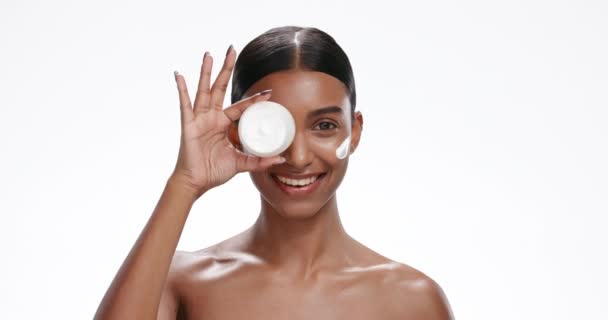 Cream, skincare and face of Indian woman for facial care, wellness and beauty on studio white background. Dermatology, portrait and isolated person for moisturizer jar, lotion or anti aging cosmetics. - Footage, Video