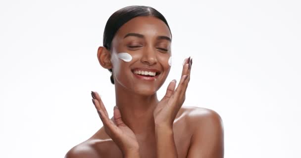 Face of happy Indian woman with cream for skincare, wellness and facial cosmetics on white background studio. Spa, beauty and portrait of isolated person with moisturizer, lotion and anti aging creme. - Footage, Video