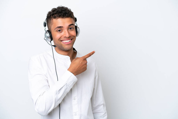 Telemarketer Brazilian man working with a headset isolated on white background pointing finger to the side - Photo, Image