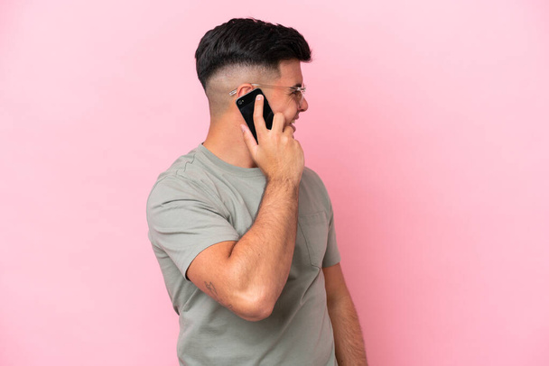 Young caucasian handsome man isolated on pink background keeping a conversation with the mobile phone with someone - Photo, Image