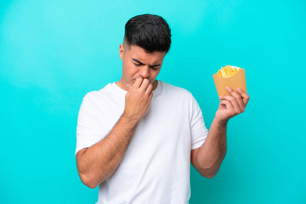 Young caucasian man catching french fries isolated on blue background having doubts - Foto, immagini