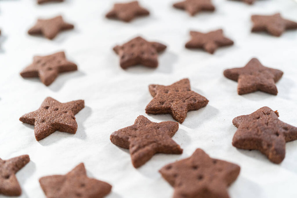 Raffreddamento di cracker al cioccolato graham appena sfornati a forma di stella sulla teglia rivestita con carta pergamena. - Foto, immagini