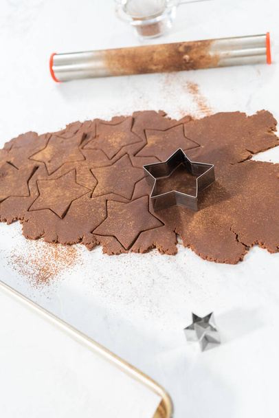 Cięcie czekoladowych krakersów w kształcie gwiazdy z ciasta nożem do ciastek. - Zdjęcie, obraz
