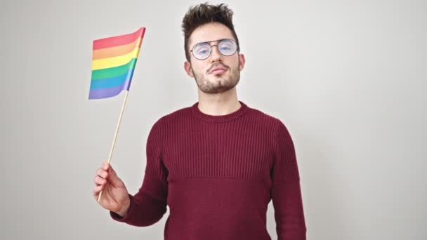 Giovane uomo ispanico sorridente fiducioso tenendo bandiera arcobaleno su sfondo bianco isolato - Filmati, video