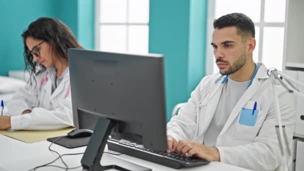 診療所で笑顔のメモを取るコンピュータを使用する男女の医師 - 映像、動画
