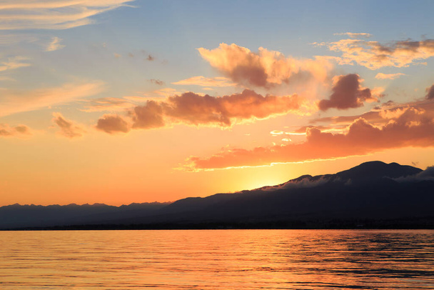 Krásný oblačný západ slunce nad mořem a horami. Jasná obloha v paprscích oranžového slunce. přírodní - Fotografie, Obrázek