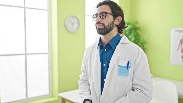 Junger hispanischer Arzt steht mit ernstem Gesichtsausdruck mit Stethoskop in der Klinik - Filmmaterial, Video