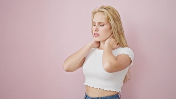 Mujer rubia joven que sufre de dolor cervical sobre fondo rosa aislado - Imágenes, Vídeo