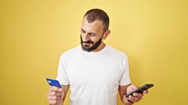 Mladý hispánec muž nakupování s smartphonem a kreditní kartou přes izolované žluté pozadí - Záběry, video
