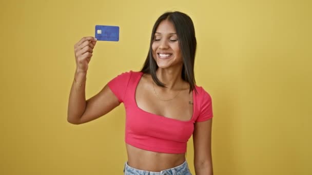 Mladá latinská žena usmívající se sebevědomě drží kreditní kartu slaví přes izolované žluté pozadí - Záběry, video