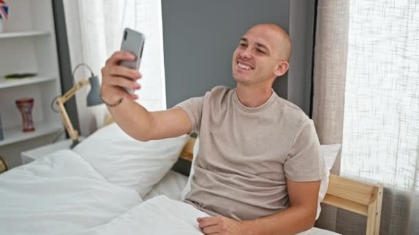 Νεαρός Ισπανόφωνος κάνει selfie από smartphone κάθεται στο κρεβάτι στο υπνοδωμάτιο - Πλάνα, βίντεο