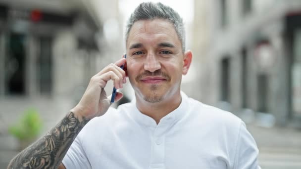 Νεαρός Ισπανόφωνος άντρας χαμογελάει με αυτοπεποίθηση μιλώντας στο smartphone στο δρόμο - Πλάνα, βίντεο