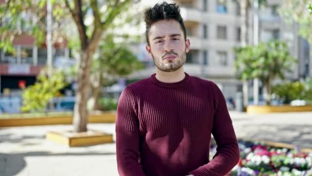 Fiatal spanyol férfi áll komoly arccal és keresztbe tett kézzel gesztussal a parkban - Felvétel, videó