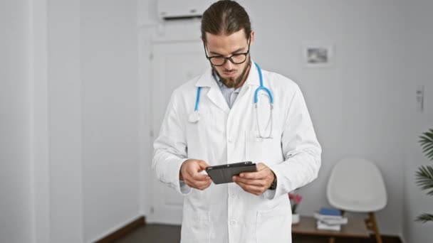 Νεαρός Ισπανός γιατρός που χρησιμοποιεί touchpad χαμογελώντας στην αίθουσα αναμονής της κλινικής - Πλάνα, βίντεο