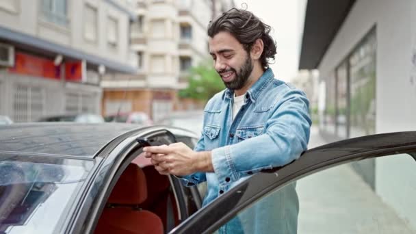 Jonge Spaanse man met behulp van smartphone leunen door de deur auto op straat - Video