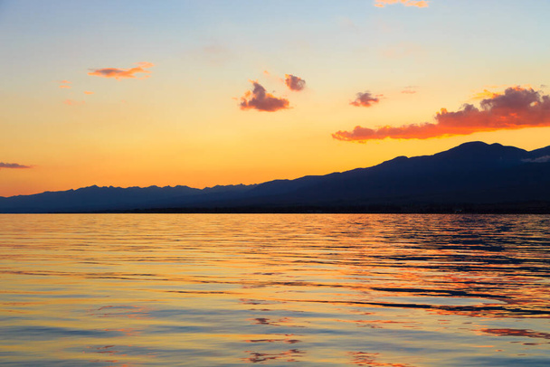 Barevný západ slunce na moři. Horské jezero v paprscích oranžového slunce. Kyrgyzstán, jezero Issyk-Kul. přírodní pozadí - Fotografie, Obrázek