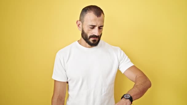 Молодий іспаномовний чоловік дивиться на годинник, напружений над ізольованим жовтим тлом - Кадри, відео