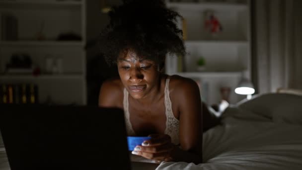 Africano americano mulher compras com laptop e cartão de crédito deitado na cama no quarto - Filmagem, Vídeo