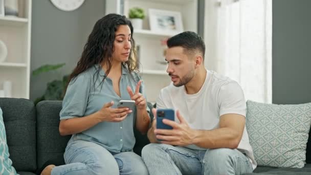mężczyzna i kobieta para za pomocą smartfonów siedzi na kanapie w domu - Materiał filmowy, wideo