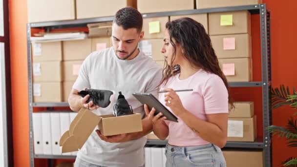 Man and woman ecommerce business workers using touchpad unpacking sneakers on cardboard box at office - Footage, Video