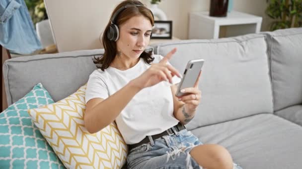Mujer joven escuchando música sentada en el sofá bailando en casa - Metraje, vídeo