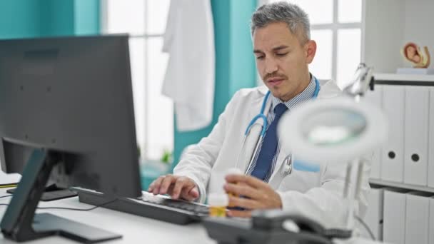 Mladý hispánec muž lékař pomocí počítače drží pilulky na klinice - Záběry, video