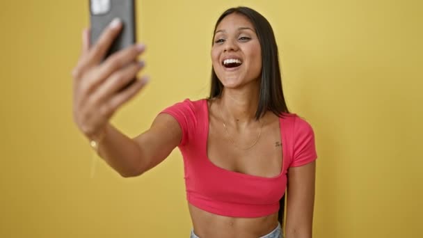 Fiatal latin nő mosolygós magabiztos birtoklás video hívás izolált sárga háttér - Felvétel, videó