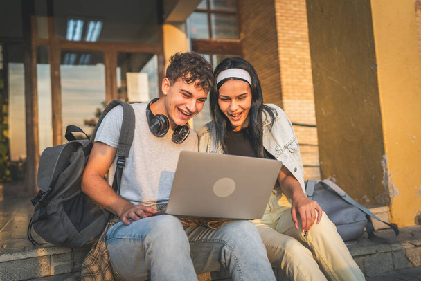 dospívající pár kavkazský muž a žena přítel a přítelkyně studenti muž a žena sledovat video film na notebooku ve škole, zatímco sedět venku v slunečný den šťastný úsměv bavte se on-line - Fotografie, Obrázek