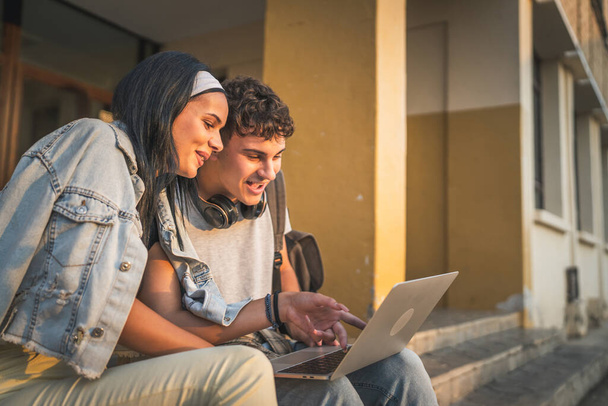 tizenéves pár kaukázusi férfi és nő barát és barátnő diákok férfi és nő videó filmet nézni laptop számítógépen az iskolában, miközben ülni szabadban napsütéses nap boldog mosoly érezd jól magad online - Fotó, kép