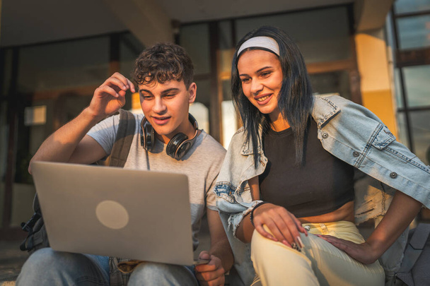tizenéves pár kaukázusi férfi és nő barát és barátnő diákok férfi és nő videó filmet nézni laptop számítógépen az iskolában, miközben ülni szabadban napsütéses nap boldog mosoly érezd jól magad online - Fotó, kép