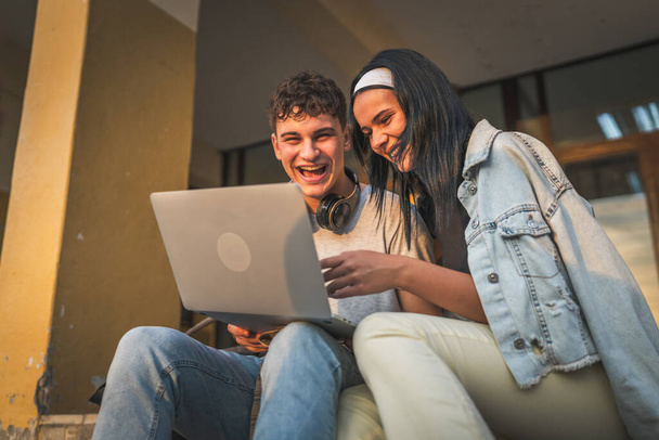 Teenager-Paar kaukasischen männlichen und weiblichen Freund und Freundin Studenten Mann und Frau Video-Film auf Laptop-Computer in der Schule ansehen, während im Freien sitzen in sonnigen Tag glücklich Lächeln Spaß haben online - Foto, Bild