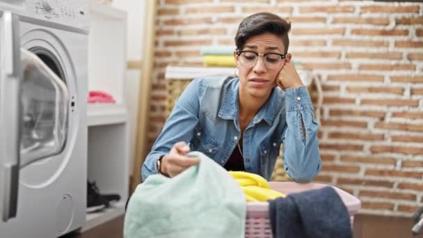 Young beautiful hispanic woman leaning on basket with clothes sadness at laundry room - Footage, Video
