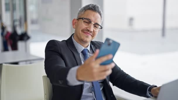 Mladý hispánec muž obchodní pracovník pomocí notebooku, aby selfie chytrým telefonem v kanceláři - Záběry, video